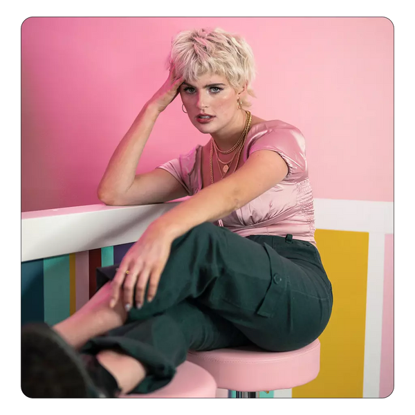 Donna con capelli biondo platino dallo stile corto e moderno, seduta in un ambiente colorato, look valorizzato da shampoo antigiallo per riflessi freddi e luminosi