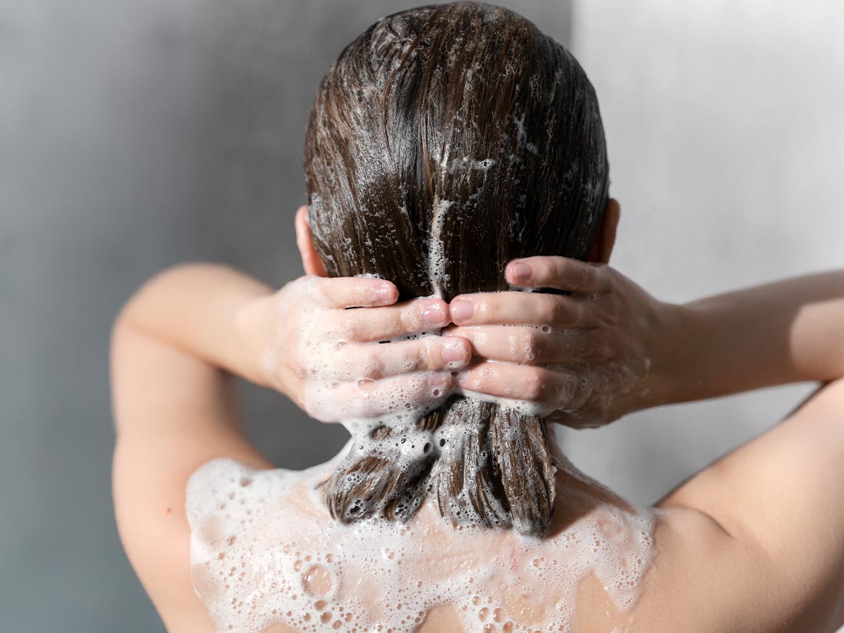 Donna che lava i capelli con shampoo anticaduta durante la doccia, trattamento per ridurre la caduta stagionale