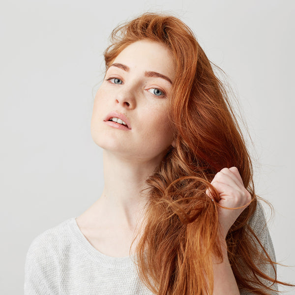 donna dai capelli rossi che si stringe i capelli, rinforzati dopo aver utilizzato uno shampoo anticaduta